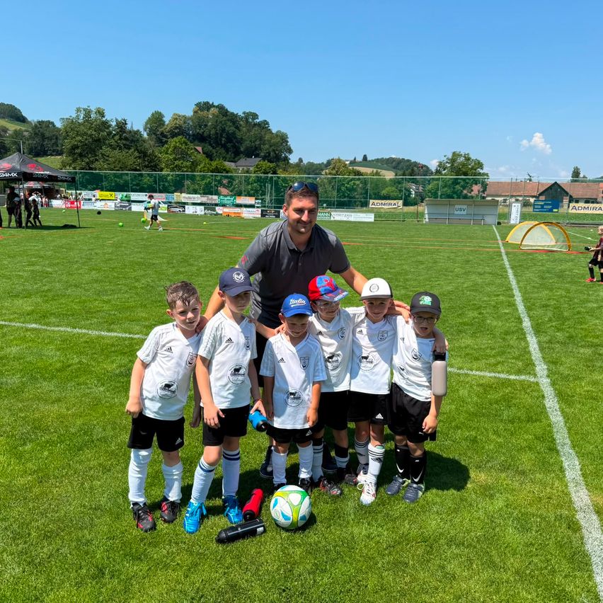 Ein Mann und sechs Jungen stehen auf einem Fußballfeld und posieren für ein Foto mit einem Fußball.