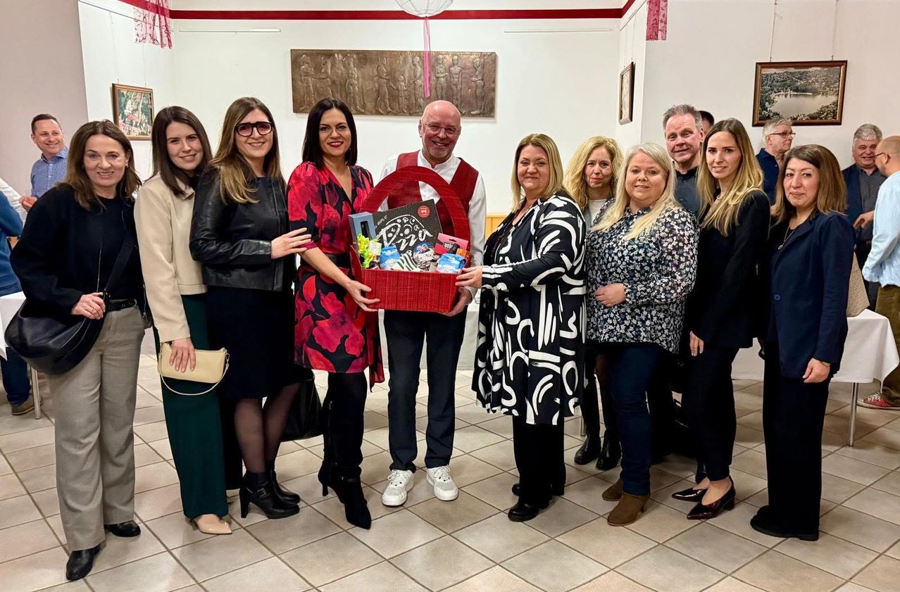 Eine Gruppe von Erwachsenen posiert für ein Foto mit einem Mann in der Mitte, der einen roten Geschenkkorb mit verschiedenen Gegenständen darin hält.