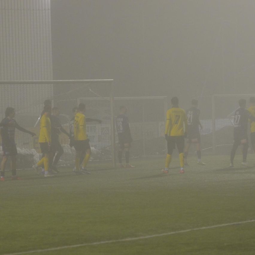 Ein Fußballspiel unter nebligen Bedingungen, mit Spielern in gelben Trikots und schwarzen Shorts in der Nähe des Tors.