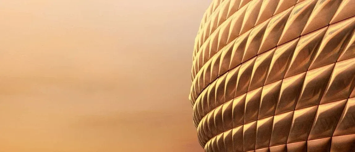 Eine goldene Struktur mit strukturierter Oberfläche. Die Textur scheint aus kleinen, rautenförmigen Paneelen zu bestehen. Der Hintergrund ist eine weiche, gelblich-orange Farbe, was möglicherweise auf einen Sonnenuntergang hindeutet.