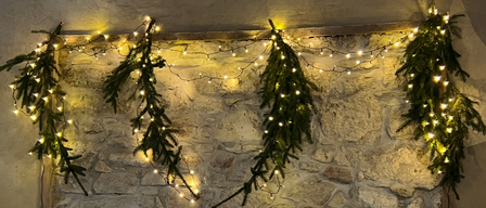 Eine Steinmauer mit drei beleuchteten Tannengirlanden. Die Girlanden sind von den Lichtern beleuchtet.
