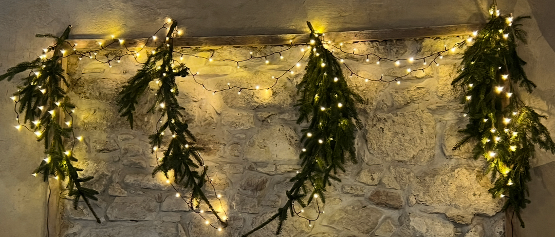 Eine Steinmauer mit drei beleuchteten Tannengirlanden. Die Girlanden sind von den Lichtern beleuchtet.