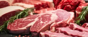 Rohes Rindfleisch ist auf einer dunklen Oberfläche angeordnet. Das Fleisch ist frisch und hat ein marmoriertes Aussehen. Einige Stücke sind teilweise mit Kräutern bedeckt.