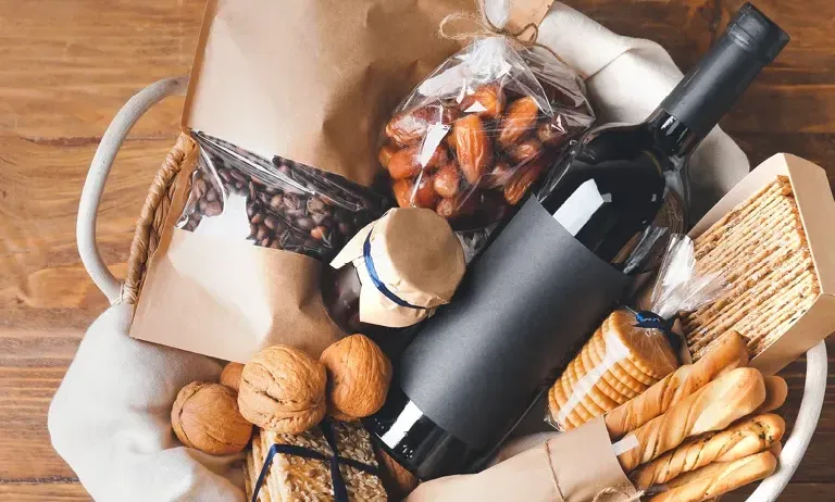 Ein Korb mit verschiedenen Lebensmitteln wie Brot, einer Flasche Wein und Nüssen auf einem Holztisch.