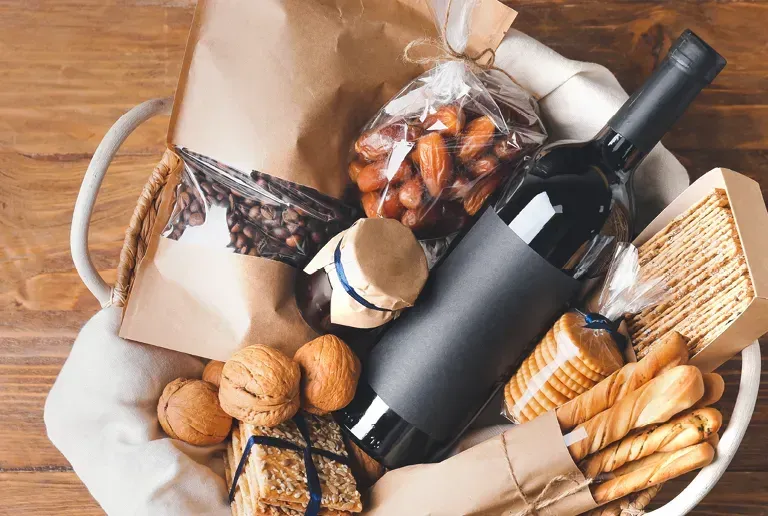 Ein Korb mit verschiedenen Lebensmitteln wie Brot, einer Flasche Wein und Nüssen auf einem Holztisch.