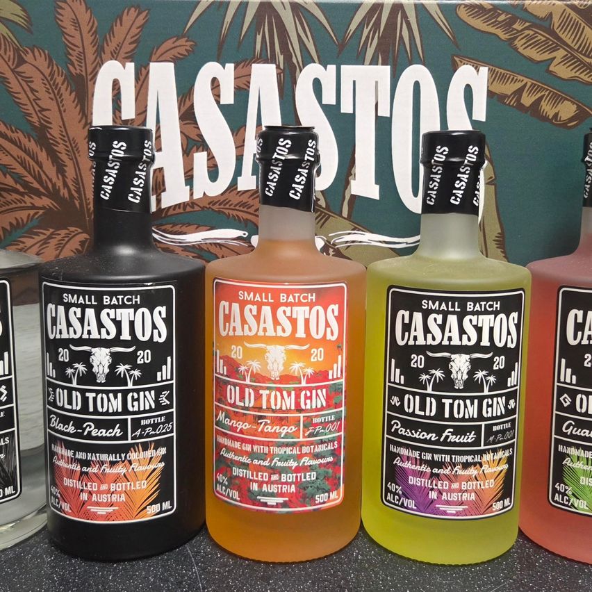 Fünf Flaschen Casastos Old Tom Gin mit verschiedenen Geschmacksrichtungen wie Black-Peach, Mango-Tango, Passion Fruit und Guava. Jede Flasche ist mit Geschmack, Alkoholgehalt und Volumen beschriftet.