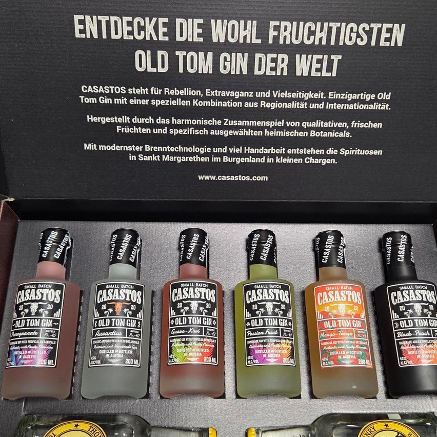 Eine schwarze Box mit mehreren Flaschen Old Tom Gin, die mit verschiedenen Geschmacksrichtungen und Zutaten beschriftet sind. Die Box enthält eine Website-Adresse und einen Slogan über die Entdeckung des geschmackvollsten Old Tom Gin der Welt.
