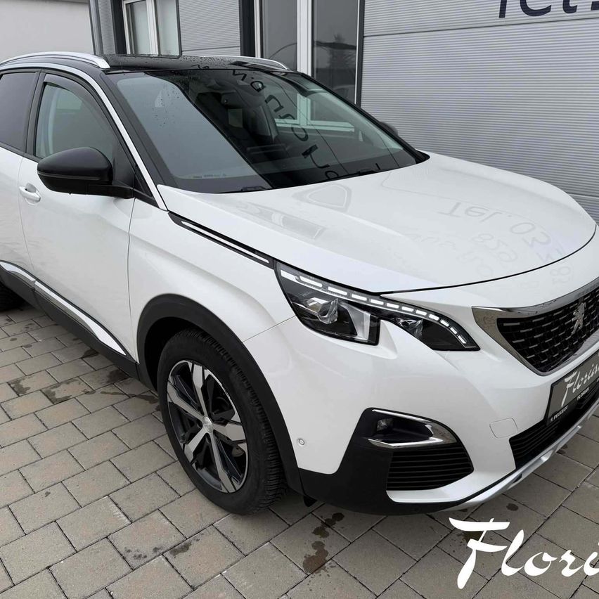 Ein weißer Peugeot SUV mit schwarzen Akzenten steht vor einem Gebäude. Das Auto hat ein schlankes Design mit einem großen Logo auf dem vorderen Stoßfänger.