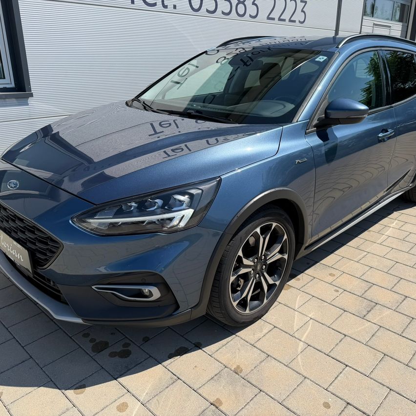 Ein blauer Ford Focus ST-Line X ist vor einem Gebäude geparkt, an dessen Wand eine Telefonnummer steht.