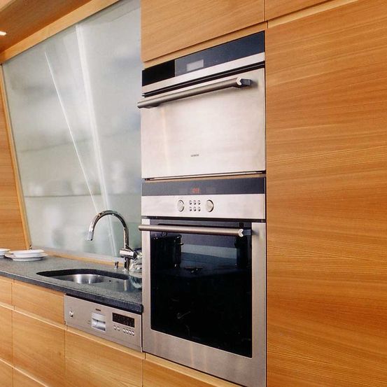 Eine moderne Küche mit Holzschränken, einem Edelstahlofen und Mikrowelle, einem Waschbecken mit Wasserhahn und einer Spülmaschine unter der Arbeitsplatte.