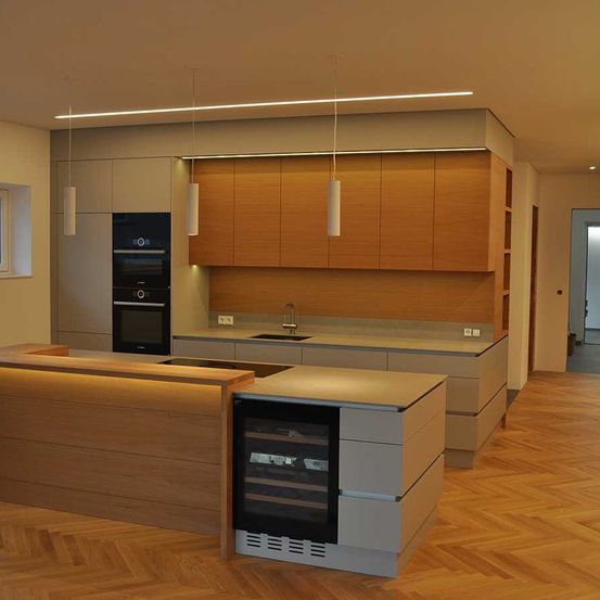 Eine moderne Küche mit Holzboden, Schränken und Geräten. Eine Insel mit Weinkühler und eine Spüle mit Wasserhahn. Hängende Lampen über der Arbeitsplatte.