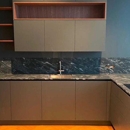 Eine moderne Küche mit Marmorarbeitsplatten, eleganten Schränken und einem stilvollen Wasserhahn. Die Wand ist blau gestrichen, und über den Schränken befindet sich ein Holzregal.