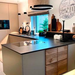 Eine moderne Küche mit Holzschränken, einer Granitarbeitsplatte und einer zentralen Insel. Eine große runde Deckenleuchte hängt über der Arbeitsplatte.