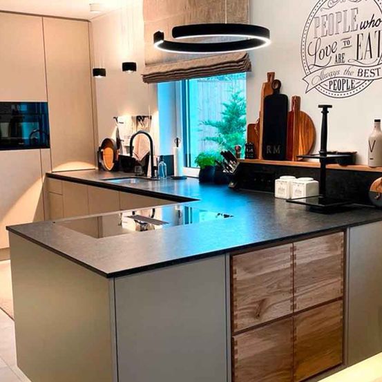 Eine moderne Küche mit Holzschränken, einer Granitarbeitsplatte und einer zentralen Insel. Eine große runde Deckenleuchte hängt über der Arbeitsplatte.