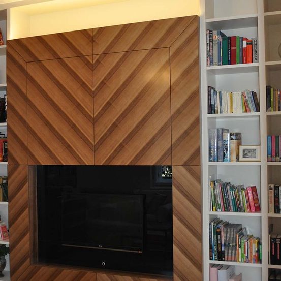 Ein Raum mit Kamin, ausgestattet mit einer großen hölzernen Chevron-Wand, einem Flachbildfernseher und weißen Regalen, gefüllt mit Büchern und einem kleinen Bilderrahmen.