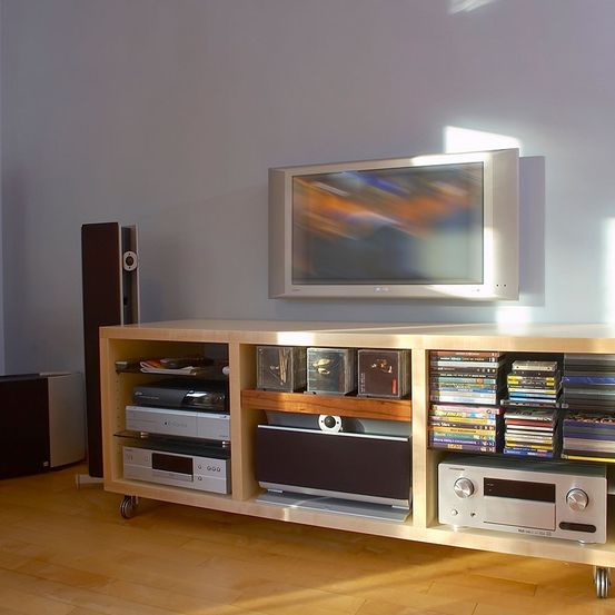 Ein modernes Entertainment-Center mit einem Flachbildfernseher an der Wand, einem Holz-Media-Ständer mit Lautsprechern und einer Vielzahl von elektronischen Geräten und Medien, die auf Regalen organisiert sind.