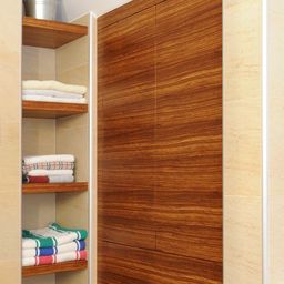 Ein Badezimmer mit Holzregalen und gefliesten Wänden, mit ordentlich gestapelten Handtüchern und einer Holzschranktür.