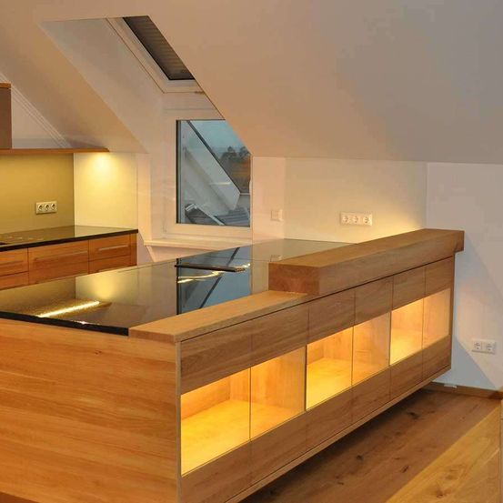 Eine moderne Küche mit einer hölzernen Insel, einer Glasplatte und LED-Beleuchtung. Die Küche hat ein Dachfenster und ein Fenster mit Blick nach draußen.