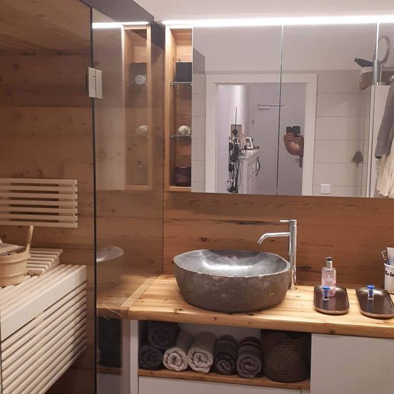 Ein Badezimmer mit einem Holz-Countertop, einem großen Steinwaschbecken und einem Spiegel, der einen Raum mit Holzwänden und Regalen reflektiert.
