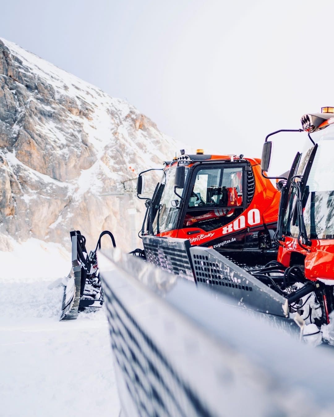 Ein roter Schneepflug mit der Nummer 800 steht im Schnee, mit einem schneebedeckten Berg im Hintergrund.