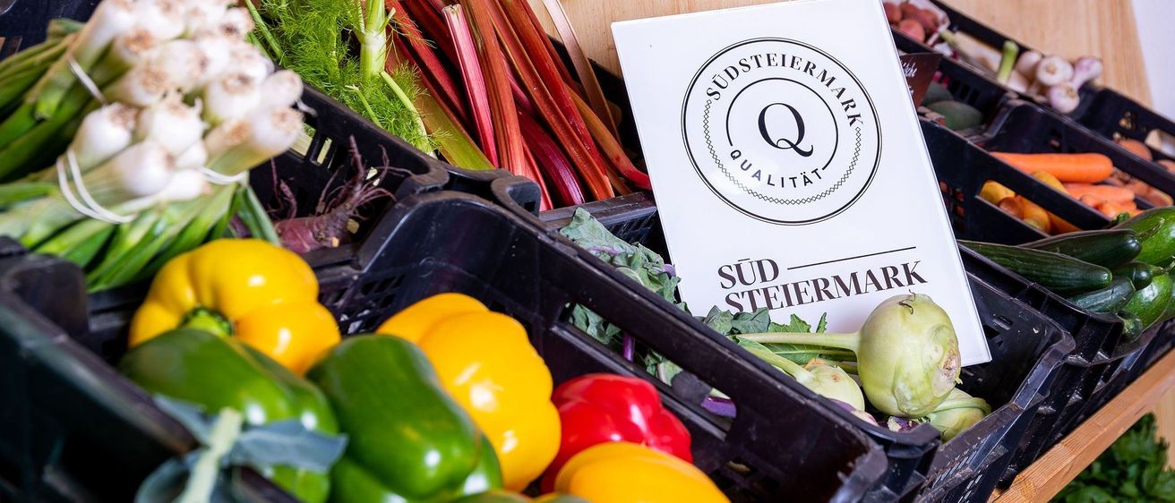 Frische Gemüse, einschließlich Paprika, Brokkoli und Rüben, sind in Körben mit einem 'Südsteiermark Qualität'-Schild auf einem Markt ausgestellt.