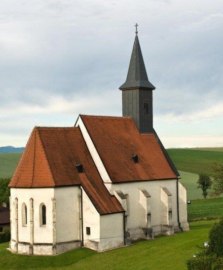 Eine alte weiße Kirche mit einem braunen Dach und einem Turm steht auf einem grünen Feld unter einem bewölkten Himmel.