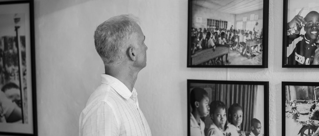 Ein Mann in einem weißen Hemd schaut auf ein gerahmtes Foto von Kindern im Klassenzimmer.