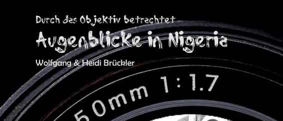 Ein schwarz-weißes Bild eines Kindes durch ein 50mm-Objektiv, lächelnd und eine gebogene Metallstange haltend. Es ist Teil eines Fotoprojekts mit dem Titel 'Augenblicke in Nigeria' von Wolfgang und Heidi Brückler.