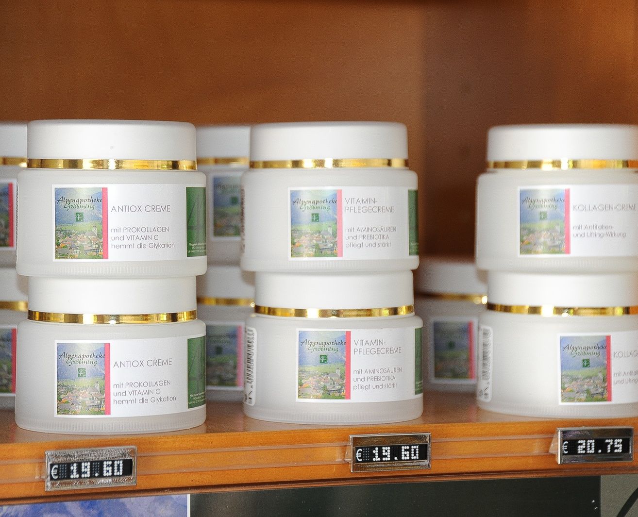 Ein Regal mit mehreren Gläsern von Hautpflegeprodukten. Die Gläser haben goldfarbene Deckel und weiße Körper. Die Gläser sind mit 'ANTIOX CREME' und 'VITAMIN-PFLEGECREME' beschriftet. Der Preis von 19,60 Euro wird auf einem digitalen Preisschild angezeigt.