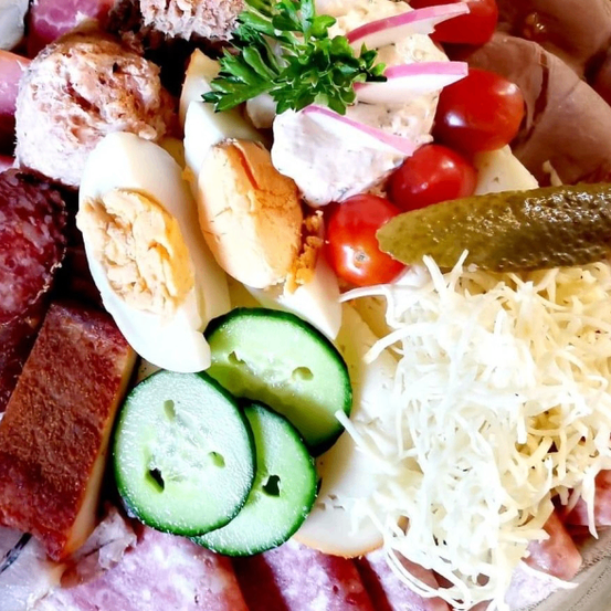 Ein Charcuterie-Brett mit verschiedenen Fleischsorten, Käse, Gurken, Tomaten, Eiern und einem Eingelegten.