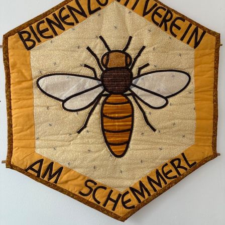 Ein sechseckiges Banner mit einer Bienenillustration in der Mitte. Es steht Bienenzuchtverein oben und Am Schmemerl unten. Das Banner ist beige und braun.