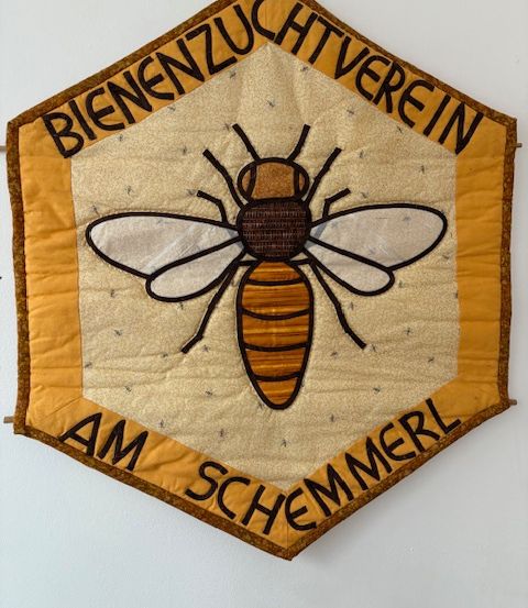 Ein sechseckiges Banner mit einer Bienenillustration in der Mitte. Es steht Bienenzuchtverein oben und Am Schmemerl unten. Das Banner ist beige und braun.