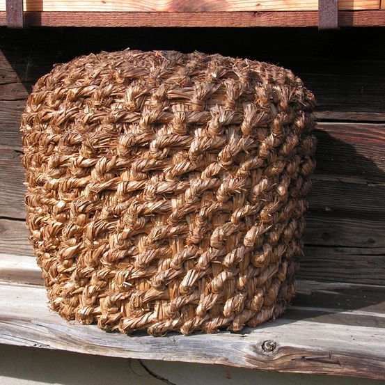 Ein gewebter runder Gegenstand mit einer strukturierten Oberfläche aus Stroh oder ähnlichem Material steht auf einem Holzregal.