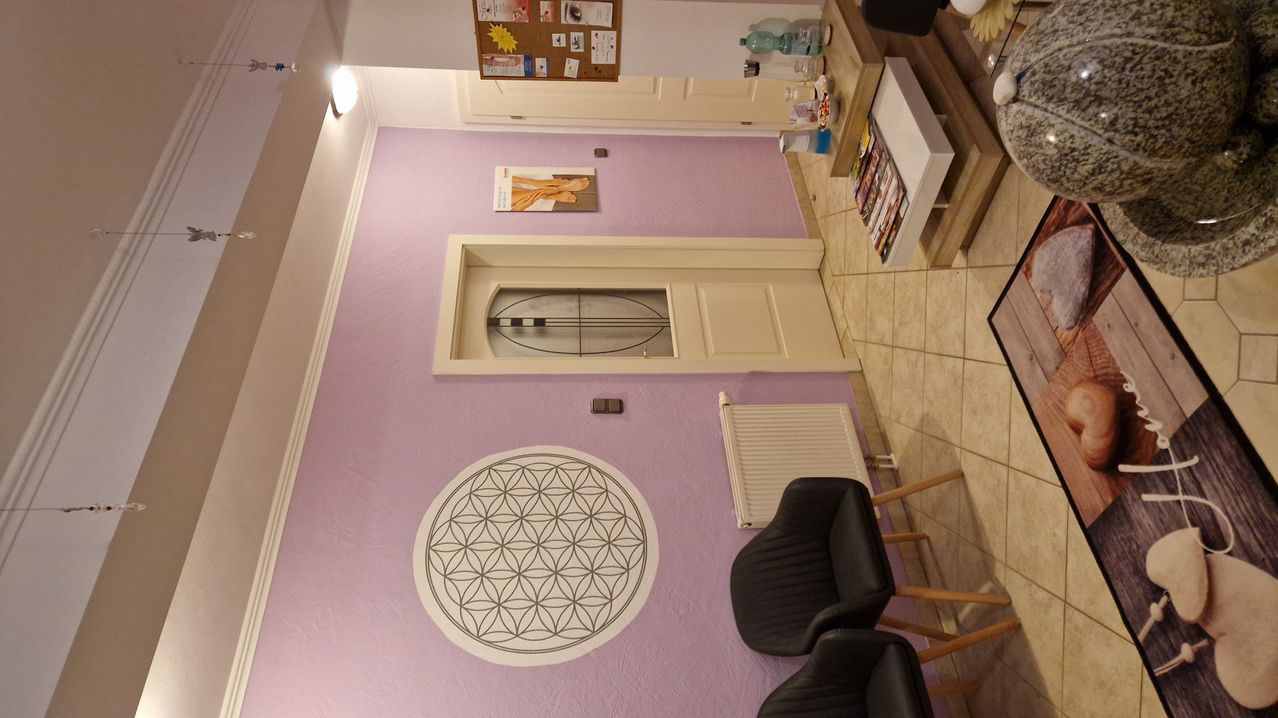 Eine Vogelperspektive eines Innenraums mit lila Wänden. Es gibt ein kreisförmiges Blumendesign an der Wand und zwei schwarze Stühle. Ein weißer Heizkörper befindet sich auf der rechten Seite des Raumes.