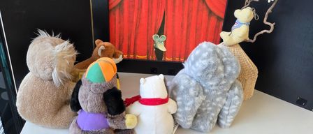 Ein gerahmtes Bild einer Bühne mit rotem Vorhang und einer Maus dahinter, umgeben von mehreren Stofftieren.