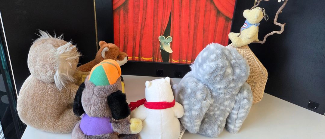 Ein gerahmtes Bild einer Bühne mit rotem Vorhang und einer Maus dahinter, umgeben von mehreren Stofftieren.