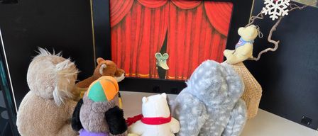 A collection of stuffed animals sits in front of a black frame with a red curtain backdrop and a silhouette of a mouse.