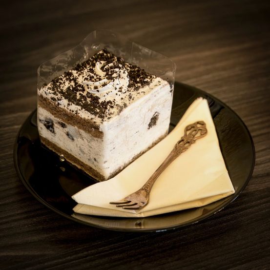 Ein Stück Kuchen mit Schokoladenkrümeln und Schlagsahne auf einem schwarzen Teller, begleitet von einer Gabel auf einem Serviettentuch.