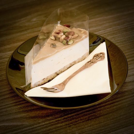 Ein Stück Pistazien-Käsekuchen mit einer Gabel auf einem Serviettentuch auf einem Holztisch.