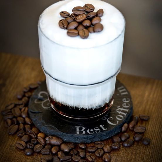 Ein Kaffeegetränk mit Schlagsahne und Kaffeebohnen, auf einem Holzuntersetzer mit den Worten 'Best Coffee in'.