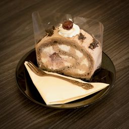 Ein Schokoladenkuchen mit Schlagsahne und einer Kirsche auf einem schwarzen Teller mit einer Gabel und einem Serviettentuch.