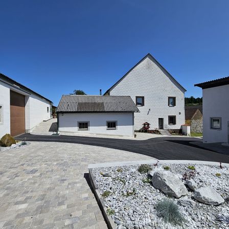 Ein modernes architektonisches Design mit drei weißen Häusern, Einfahrten und einem gepflasterten Weg. Das größte Haus hat ein graues Dach und Ziegelwände.