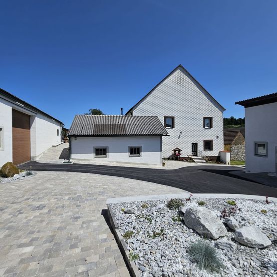 Ein modernes architektonisches Design mit drei weißen Häusern, Einfahrten und einem gepflasterten Weg. Das größte Haus hat ein graues Dach und Ziegelwände.