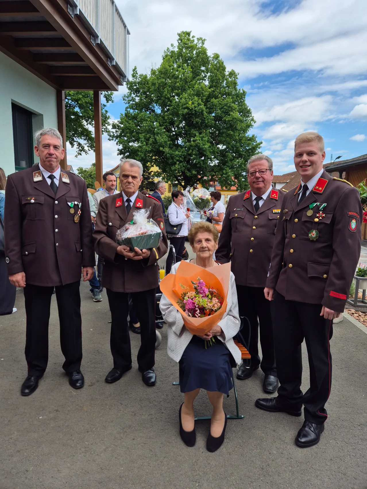 Vier Männer in Uniform stehen neben einer Frau, die einen Blumenstrauß hält, wahrscheinlich bei einer formellen Veranstaltung.