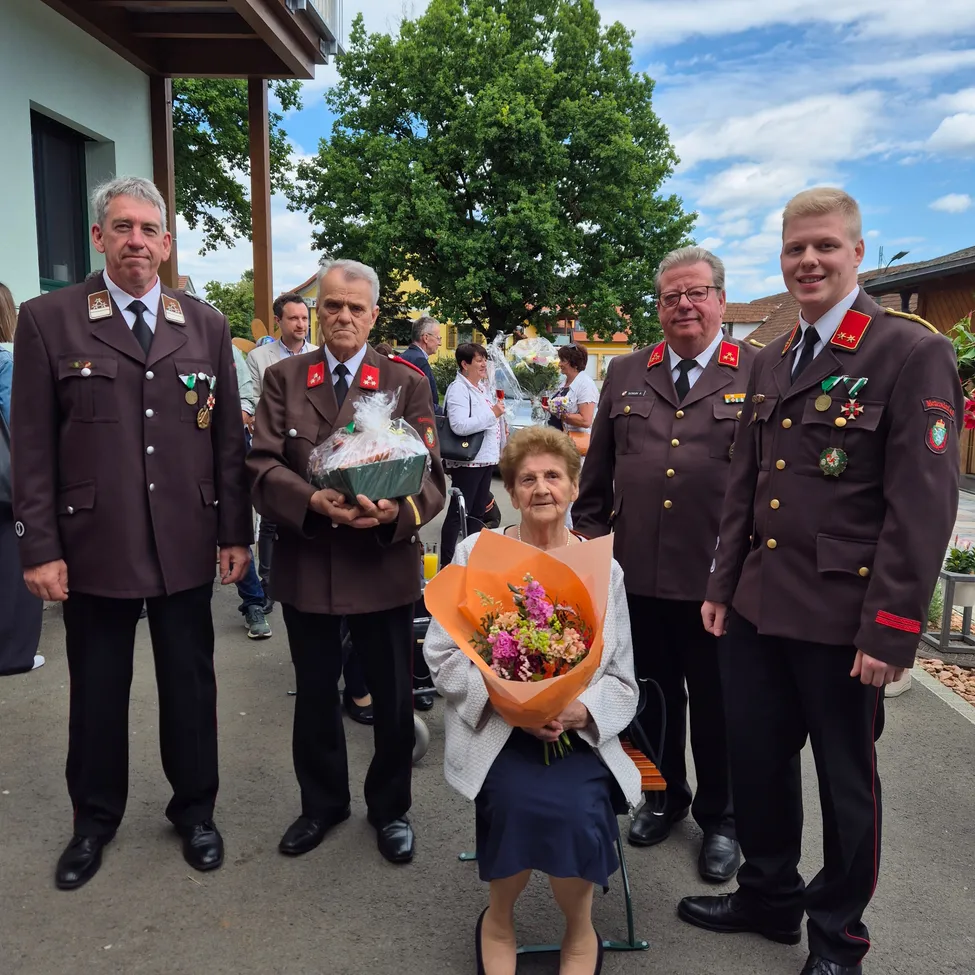 Vier Männer in Uniform stehen neben einer Frau, die einen Blumenstrauß hält, wahrscheinlich bei einer formellen Veranstaltung.