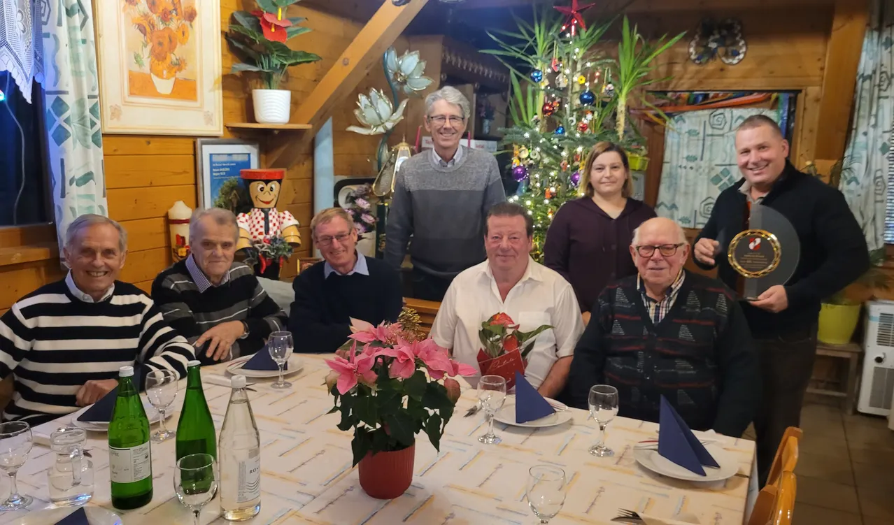 Eine Familie versammelt sich zu einem festlichen Abendessen um einen mit Blumen und einem Weihnachtsbaum geschmückten Tisch, wobei eine Holzwand und Dekorationen im Hintergrund zu sehen sind.
