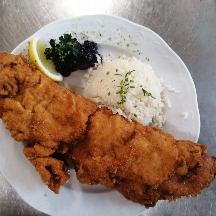 Ein weißer Teller mit knusprig gebratenem Fisch, einer Beilage weißen Reis, einer Zitronenscheibe und einer grünen Garnierung.