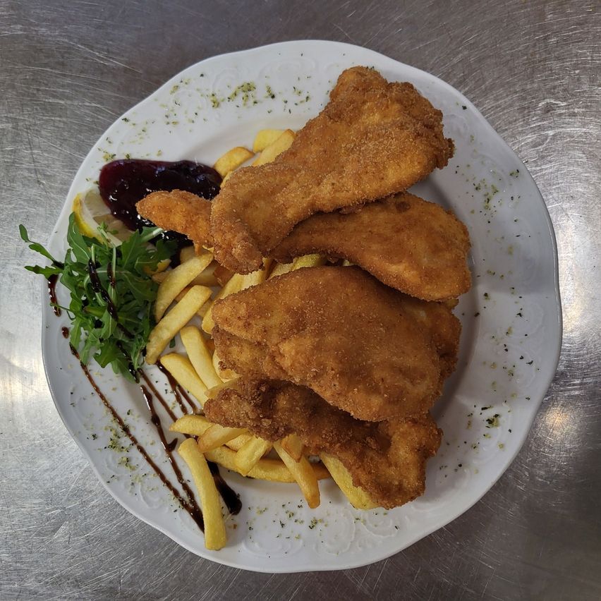 Ein Teller mit knusprigen frittierten Fischstücken und goldbraunen Pommes Frites, garniert mit einer Zitronenscheibe und grünen Blättern, serviert mit einer Beilage aus roter Beerensauce.