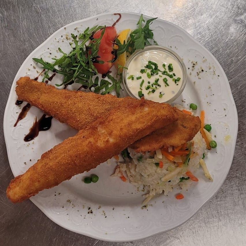 Ein weißer Teller mit gebratenem Fisch, Salat, einer Sauce und Gemüse.