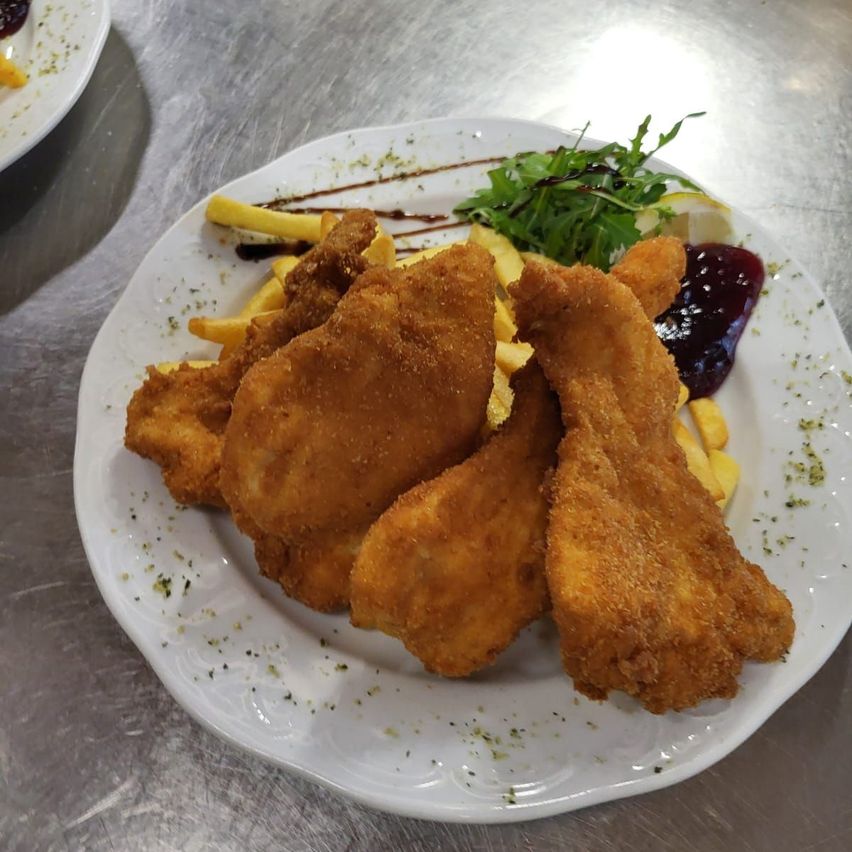 Ein Teller mit gebratenem Hähnchen, Pommes und grünen Beilagen steht auf einer silbernen Oberfläche.
